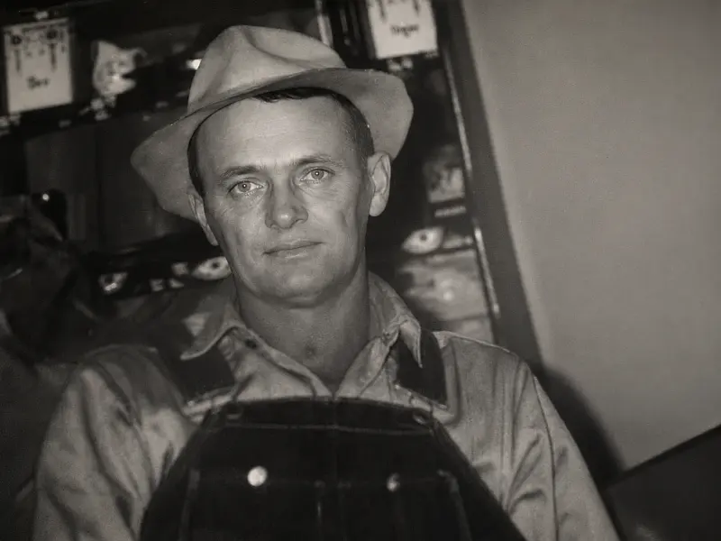 Grainy black and white photo of a farmer in overalls and hat with a mule and plow during the Great Depression